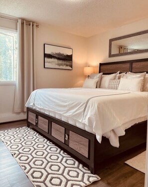 Une chambre à coucher avec un lit, une lampe de chevet, un tableau encadré au mur et un tapis à motifs.