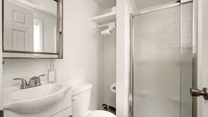A bathroom with a white sink, toilet, and a glass shower enclosure. - One bedroom duplex in desirable Park Hill (Fort Smith)