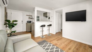 A modern living room with a sofa, a TV mounted on the wall, and a kitchen area in the background. - One bedroom duplex in desirable Park Hill (Fort Smith)
