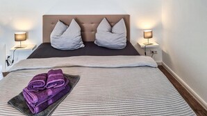 A neatly made bed with striped bedding, two pillows, and a folded purple towel on a dark-colored pillow. - Amazing apartment in Passow OT Charlottenho (Passow OT Charlottenho)