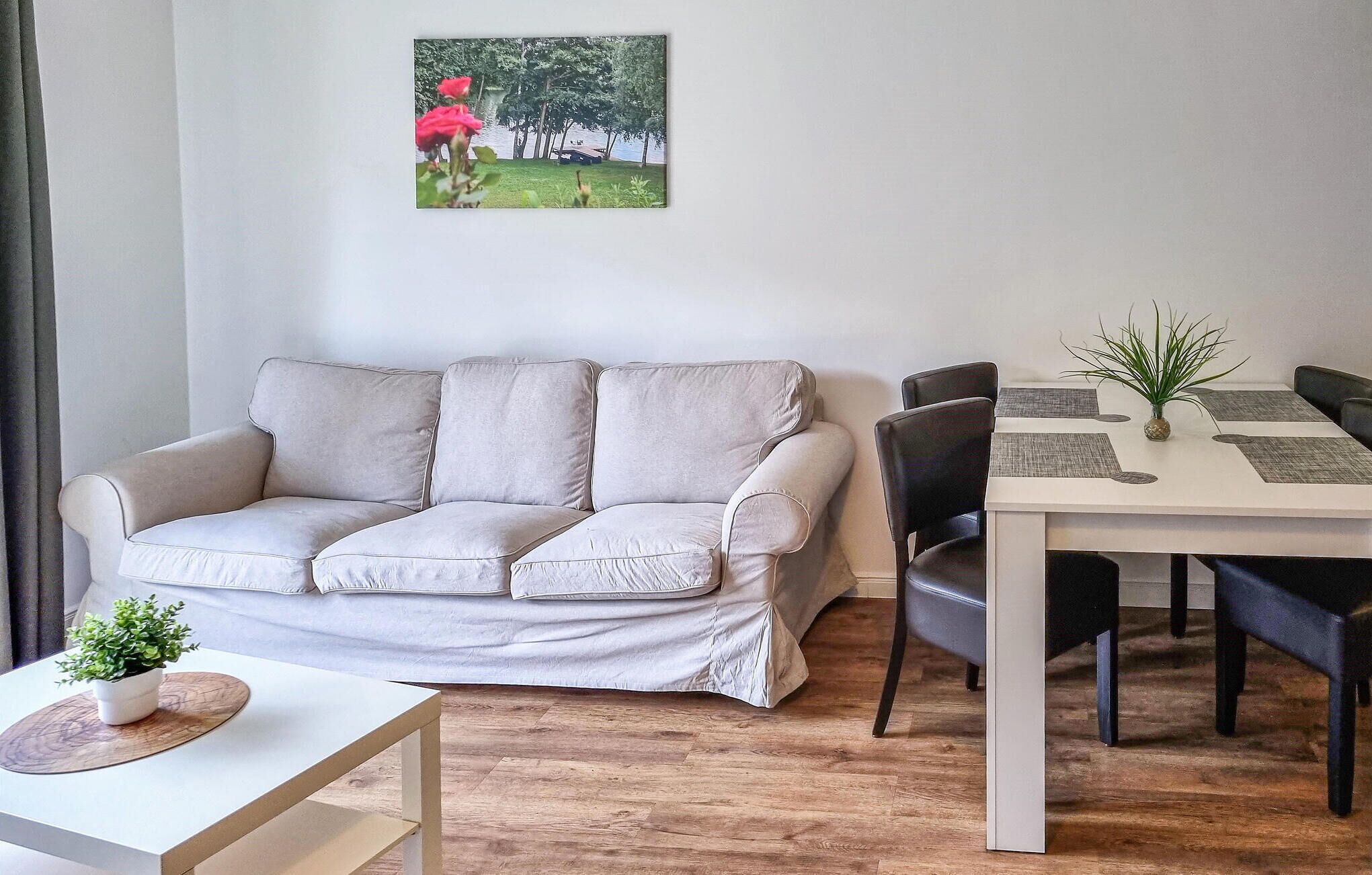 A living room with a sofa, a dining table with chairs, a small table with a plant, and a painting on the wall.