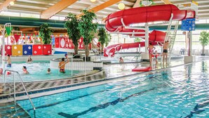 Een binnenzwembad met meerdere banen, een rode waterglijbaan en diverse voorzieningen bij het zwembad.