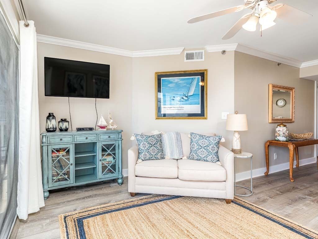 A living room with a white sofa, a teal cabinet, a framed picture, a lamp, and a ceiling fan.