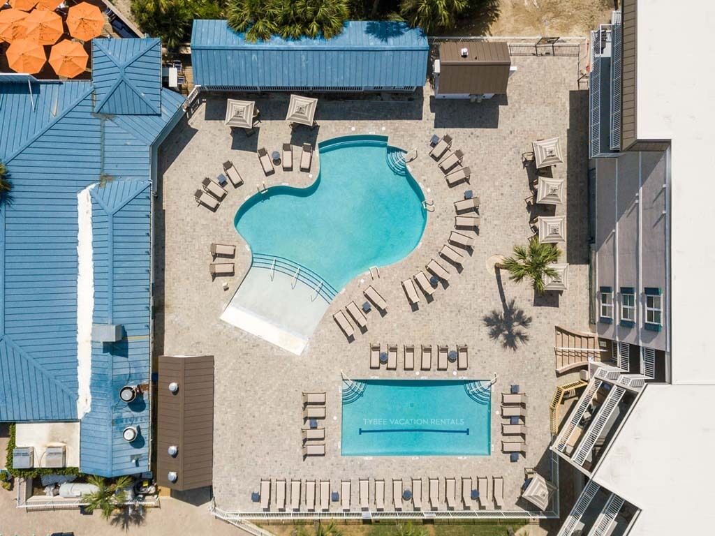 Vue aérienne d’un complexe hôtelier doté d’une piscine, de chaises longues et d’un panneau indiquant « Tybee Vacation Rentals ».