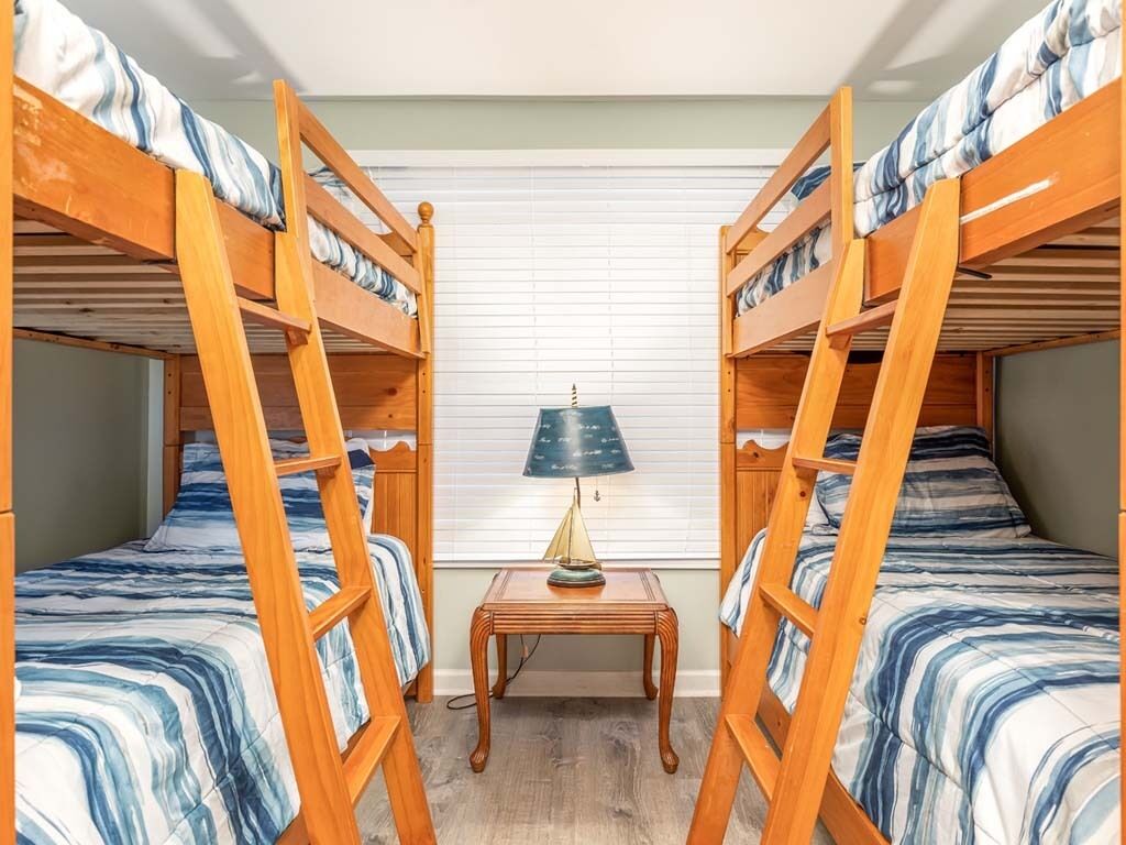 Ein Zimmer mit zwei Etagenbetten, einem kleinen Holztisch mit Lampe und einem Fenster mit Jalousien.