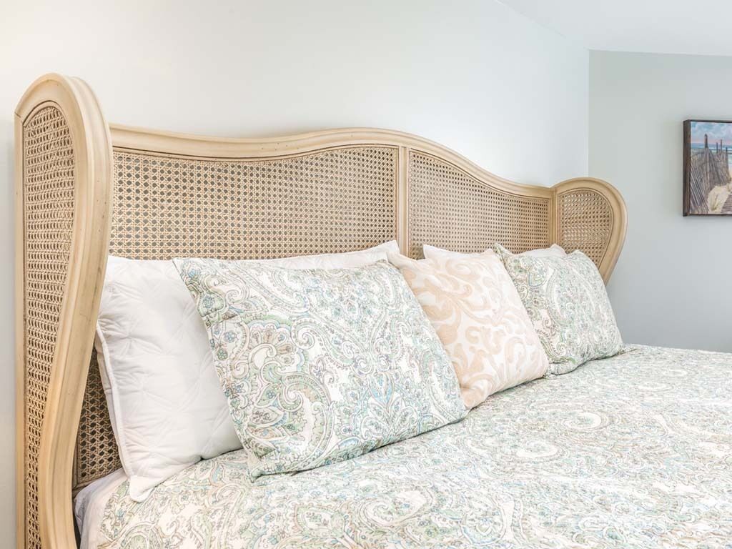 A bed with a woven headboard, patterned bedding, and a wall-mounted picture.
