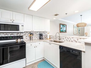 A modern kitchen with white cabinets, a microwave, stove, and dishwasher.