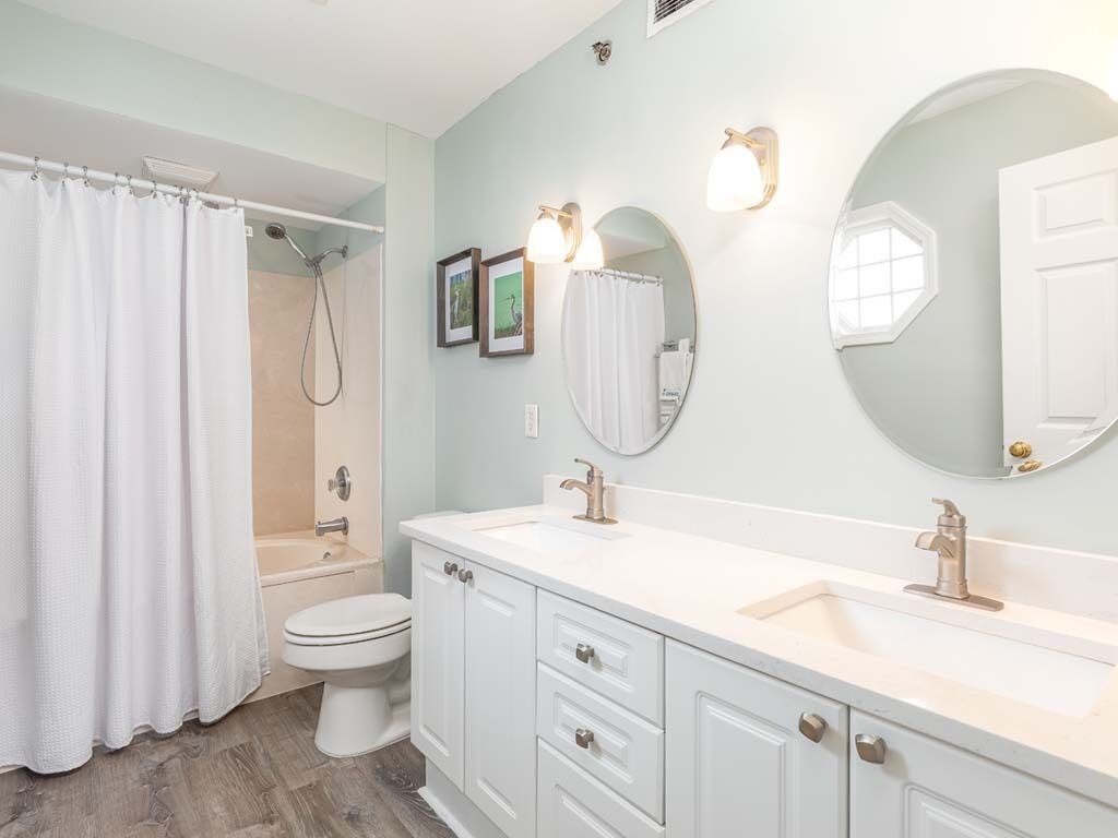A bathroom with a shower, toilet, and double sink vanity.