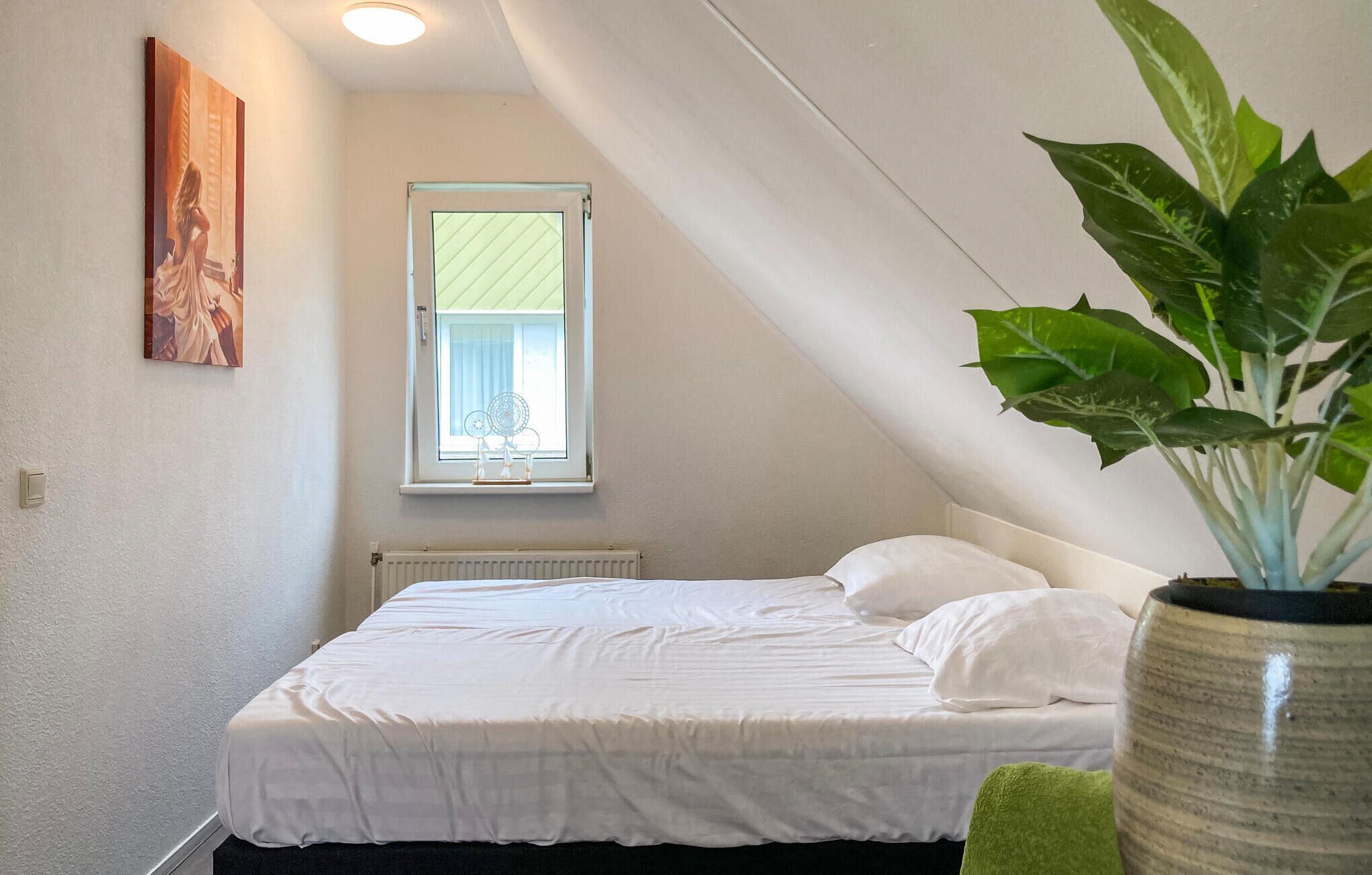 Et soveværelse med en enkelt seng, et vindue med rullegardiner, en radiator, en potteplante og et billede på væggen.