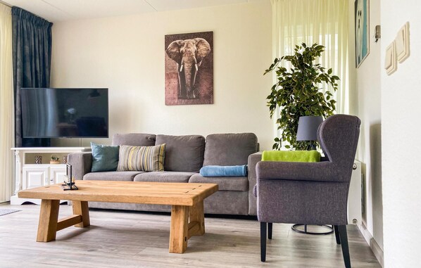 A living room with a sofa, a coffee table, a TV, a plant, and a chair.