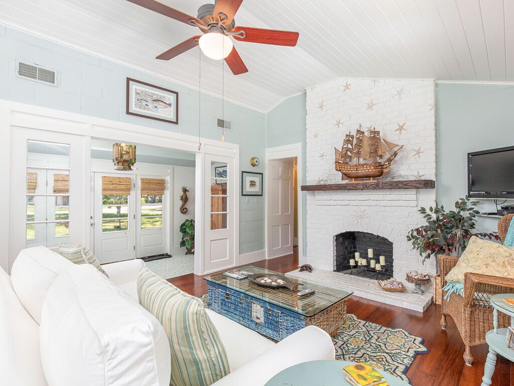 A living room with a white sofa, a coffee table, a fireplace with a ship decoration, and a ceiling fan.