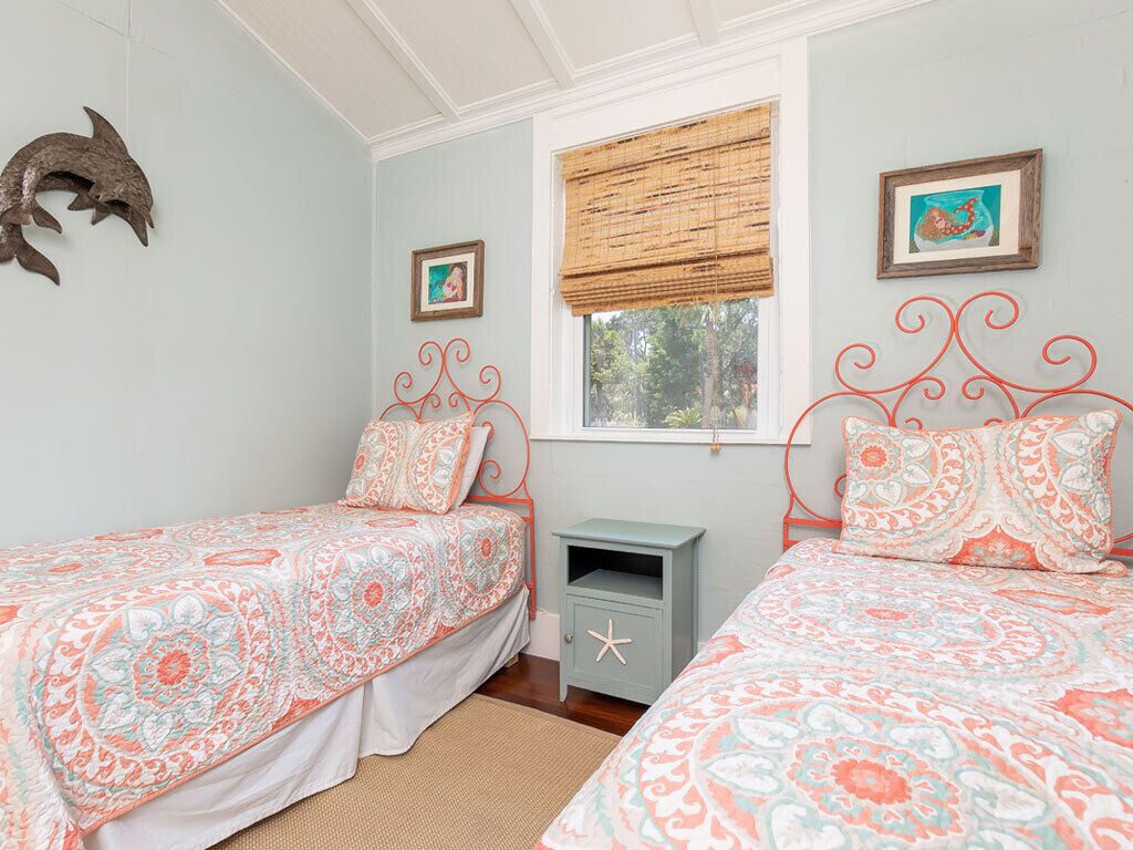 A bedroom with two beds, a small nightstand, a window with a bamboo blind, and wall art.