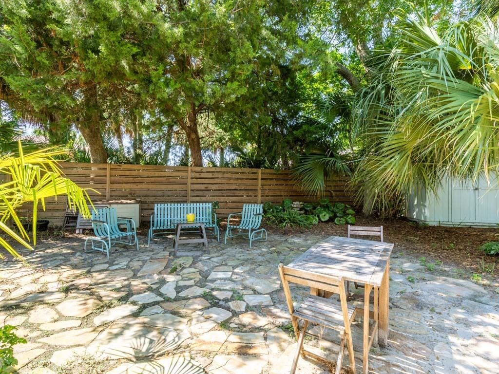 Un patio con suelo de piedra, muebles de madera y sillas verdes.