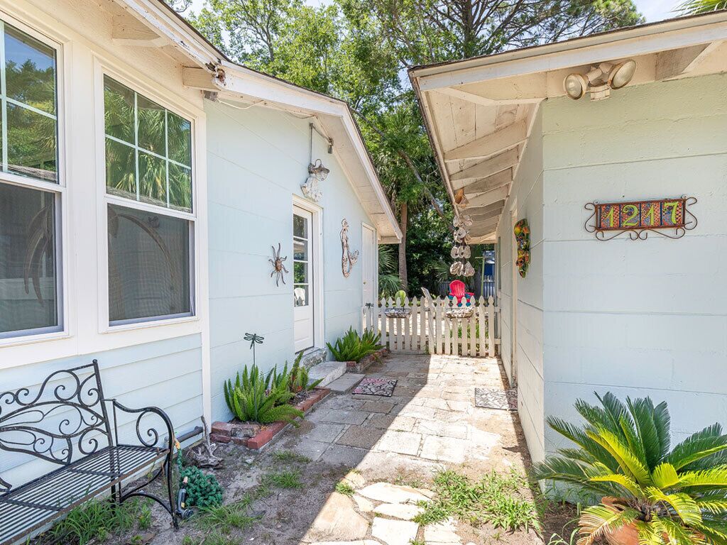 A narrow stone pathway leading to a house with a white picket fence, a bench, and various plants.