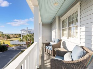 Relax on the balcony with two comfortable chairs and a small table, taking in the view of a charming house and the surrounding landscape.