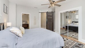 Une chambre avec un grand lit, un ventilateur de plafond, une armoire et un miroir.