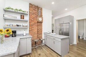 A modern kitchen with grey cabinets, a brick accent wall, and a stainless steel refrigerator. - Gorgeous 4BR Remodel - Close To Everything! (Indianapolis)