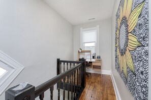 Staircase leads to a workspace with a desk and chair, surrounded by a floral patterned wall and a window with white curtains.