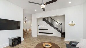 Un salon moderne doté d’un téléviseur à écran plat, d’une table basse avec un récipient décoratif, d’un canapé, d’un ventilateur de plafond et d’un escalier menant à un autre niveau.