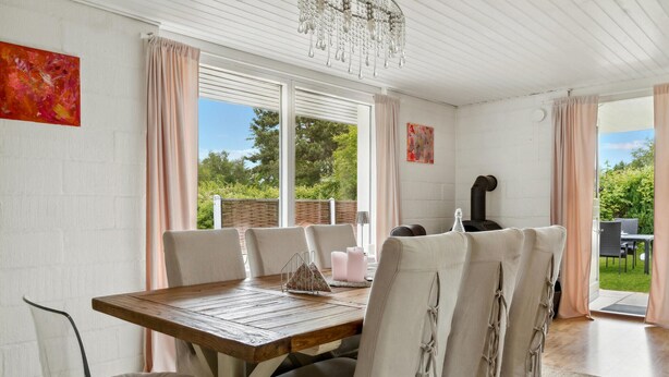 Un coin repas avec une table et des chaises en bois, de grandes fenêtres et une vue sur le jardin.