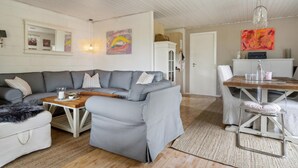 Un salon moderne avec un canapé gris, une table basse en bois et un coin repas comprenant une chaise et une table en métal.