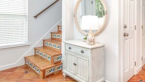 A staircase with patterned tiles, a white cabinet with a mirror, and a door. - The Cool Coconut by Tybee Vacation Rentals (Tybee Island)