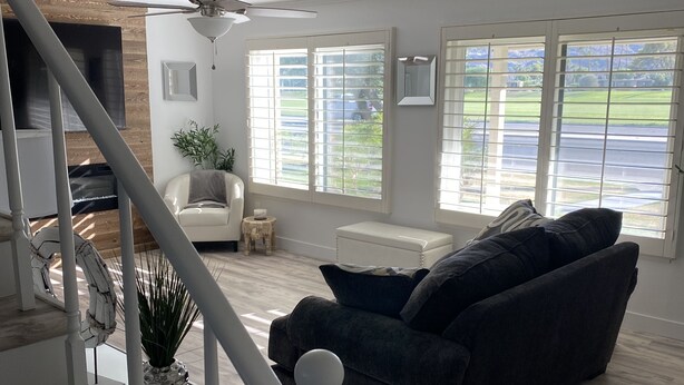 Un salón espacioso con un sofá oscuro, un sillón blanco y una escalera que lleva a un nivel superior.