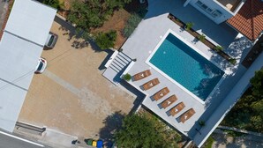 Vue aérienne d’une propriété résidentielle dotée d’une piscine, de chaises longues et d’un jardin.