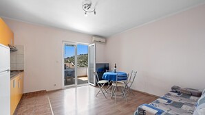 Un vaste espace de vie avec balcon, une table à manger avec des chaises, un canapé et un coin cuisine équipé d’un réfrigérateur.