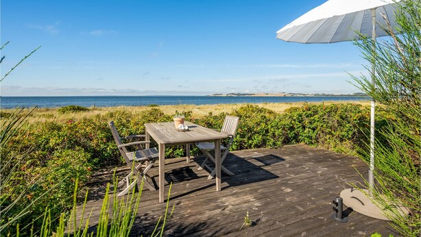 A wooden deck with a table and chairs, a white umbrella, and a view of the sea.