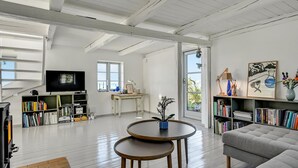 A spacious living room with a high ceiling, a television, a bookshelf, a dining table, and a sofa.