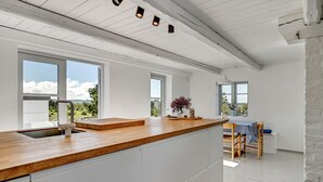 A modern kitchen with a wooden countertop, white cabinetry, and large windows offering views of the outdoors.