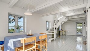A spacious room with a wooden floor, a dining table with chairs, a staircase, and large windows offering a view.