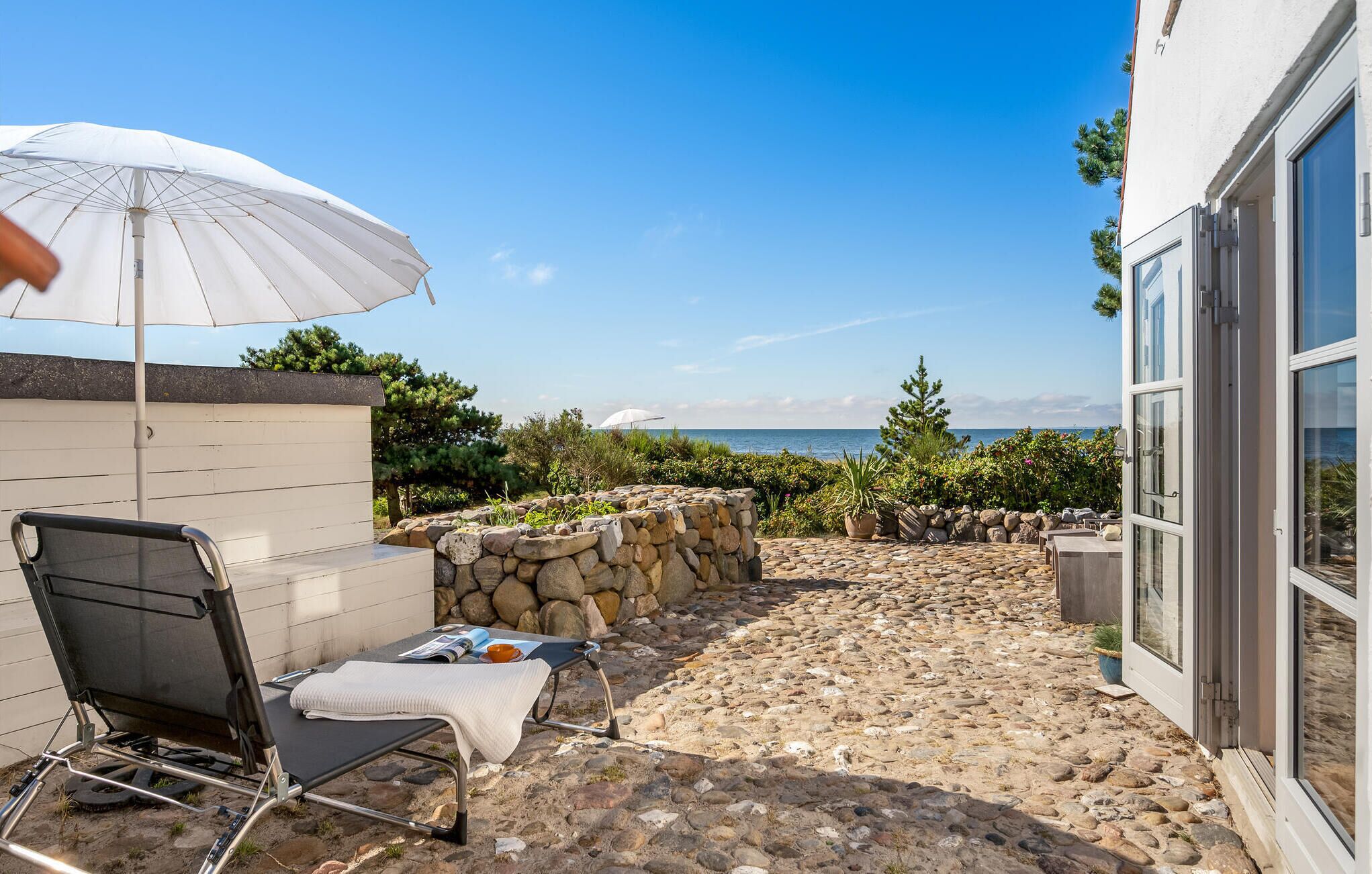 A patio with a grill, a lounge chair, and a white umbrella.