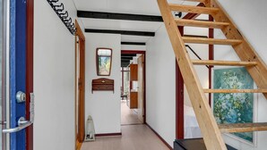 Ein schmaler Flur mit einer Holzleiter, die an einer Wand lehnt, einer Tür mit blauer Rahmung und einem Spiegel an der Wand.