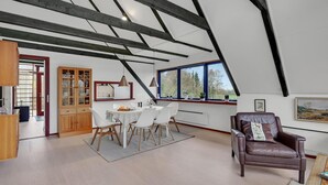 Ein geräumiges Loft mit Essbereich, einem Ledersessel und einem großen Fenster mit Blick auf Bäume.