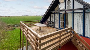 Eine Holzdielen-Terrasse mit Tisch und Stühlen, einer Satellitenschüssel und Blick auf ein grünes Feld.