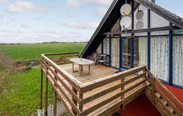 A wooden deck with a table and chairs, a satellite dish, and a view of a green field.