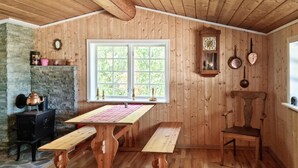 Ein Holzinnenraum mit einem großen Fenster, einem Holztisch, Bänken, einem Steinkamin und einer Wanduhr.