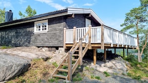Eine Holzhütte mit einer Holzterrasse, einer Treppe und einem großen Felsen davor.
