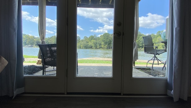 Una habitación con un amplio ventanal que da a una vista del lago. Adentro, hay una silla negra y una silla blanca cerca de la puerta.