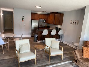 A modern living room with a dining area, a kitchen with wooden cabinets, and a small bar area.