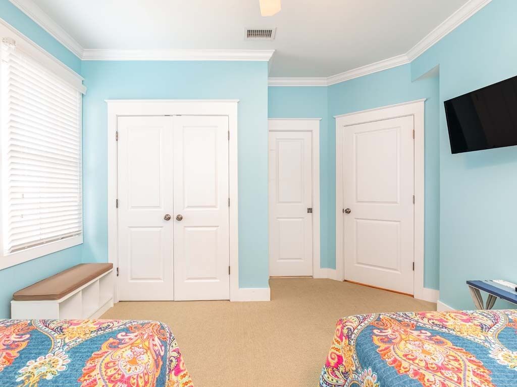 A bedroom with two beds, a bench, a TV, and three white doors.