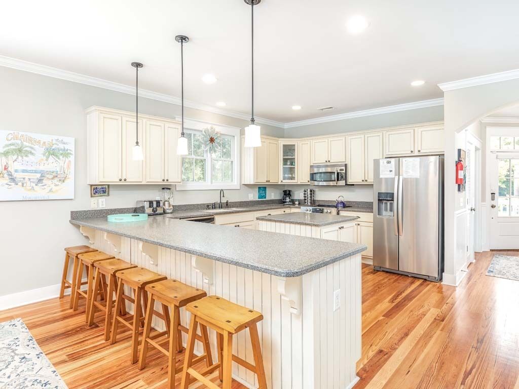 A modern kitchen with a central island, bar stools, stainless steel appliances, and pendant lighting.