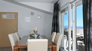A dining area with a glass table, four chairs, a candle, a clock, and a view of the sea through large windows. - 2 bedroom gorgeous apartment in Okrug Gornji (Okrug Gornji)
