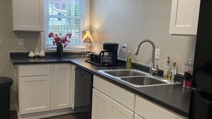 A modern kitchen with white cabinets, a black countertop, a coffee maker, and a window with a view of buildings. - Dubuque Luxury Rentals Washington Street (Dubuque)