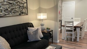 A living room with a dark sofa, a bench, a table lamp, and a dining area with chairs and a table. - Dubuque Luxury Rentals Washington Street (Dubuque)