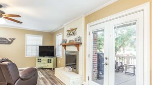 A living room with a fireplace, a television, and a sliding glass door leading to an outdoor deck. - Toes in the Sand by Tybee Vacation Rentals (Tybee Island)