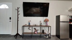 Et moderne køkken med et fladskærms-tv monteret på væggen, et trækonsolbord med dekorative genstande, og et rustfrit stål køleskab.