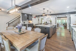 A spacious kitchen with a central island, wooden dining table, and modern pendant lighting.